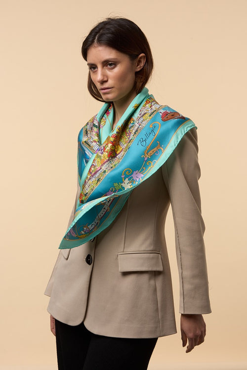 woman with cream coat wearing a blue silk scarf depicting the town of Bellagio