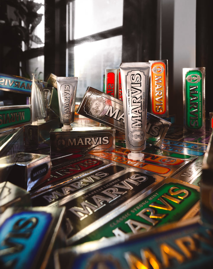 Multiple tubes of Marvis toothpaste arranged on a reflective surface with a blurred window background.